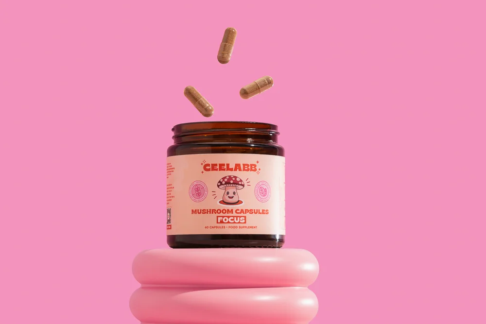 this photo has one tub of ceelabb mushroom capsules, focus blend with a peach label with a friendly mushroom on the label. the photo has a pink background and their are 3 casules falling mid air into the tub.