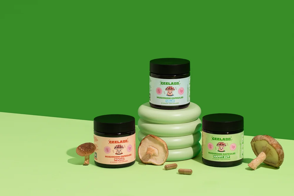 this is a photo of 3 tubs of ceelabb mushroom capsules one of each version, calm, happy gut, and focus with shiitake mushrooms against a green background